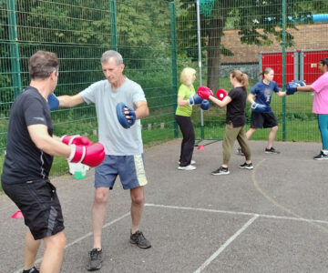 Mixed group of people exercising on outdoor court with boxing gloves and pads