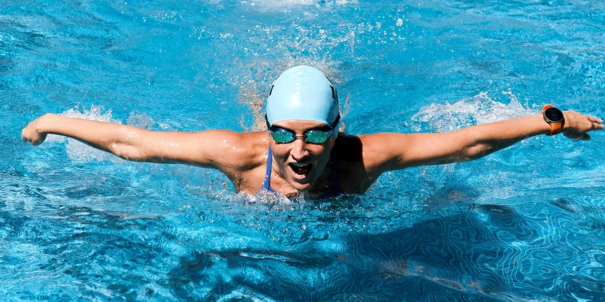 woman swimmer with swimhat and googles, arms outstretched, mid-butterfly stroke
