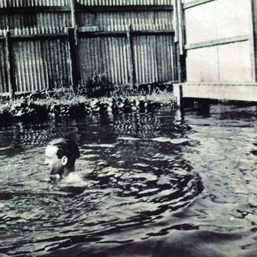 photo of boy swimming in puddle with corrugated fencing around, taken at turn of the 19th-20th century